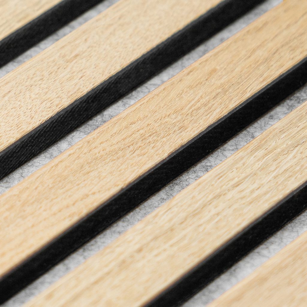 Nahaufnahme eines WoodUpp Akustikpaneels: parallele, warmtonige Eichenholz‑Lamellen mit feiner Maserung, sauber verarbeitete schwarze Fugen und darunter eine graue Filz‑Textilfläche. Detailaufnahme betont Kontrast, natürliche Holzstruktur, präzise Kanten und die hochwertige Optik der WoodUpp Wand‑ und Deckenlamellen, ideal für moderne Innenräume als akustische Lösung.