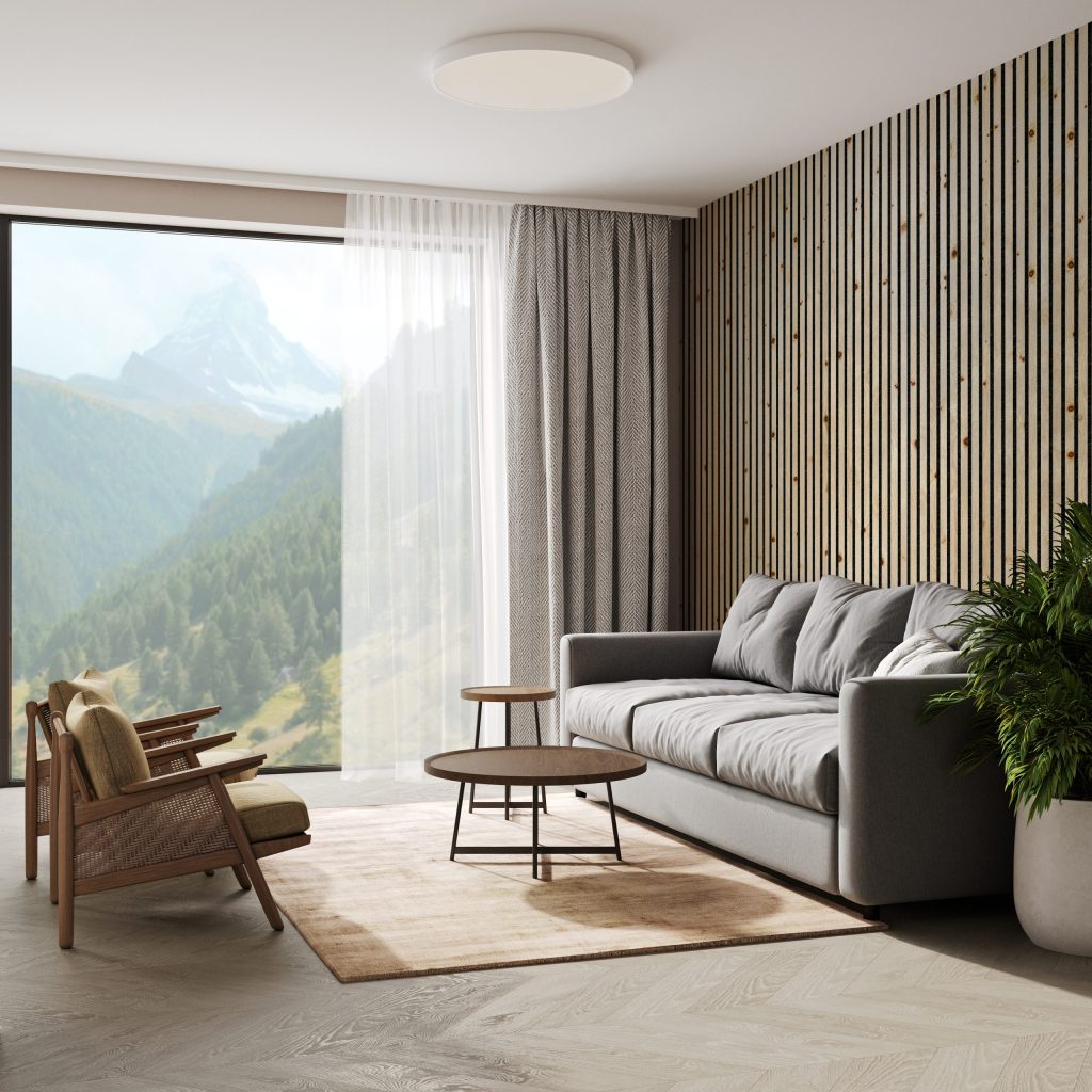 Modernes Wohnzimmer mit großer Glasfront und WoodUpp-Produkten: eine helle WoodUpp-Holzlamellenwand aus vertikalen, naturgeölten Holzlatten mit schmalen dunklen Fugen, sichtbaren Astknoten und feiner Maserung sowie ein helles WoodUpp-Fischgrätparkett. Graues Sofa, zwei Holzsessel, runde Couchtische, leichte Vorhänge und Zimmerpflanze komplettieren die Szene.
