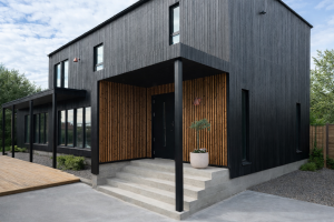 Ein modernes Haus mit schwarzer Fassade, dessen Eingangsbereich mit WoodUpp Akustikpaneelen in Eiche verkleidet ist. Die vertikalen Holzlatten der Paneele schaffen einen warmen Kontrast zur dunklen Außenwand und sorgen für eine einladende Optik.