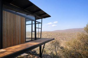 En moderne hytte med en svævende terrasse og panoramaudsigt over naturen. Facaden er beklædt med WoodUpp paneler, der har karakteristiske lodrette trælameller i en varm farvetone. Disse WoodUpp produkter tilføjer en naturlig elegance til den sorte stål- og glaskonstruktion.